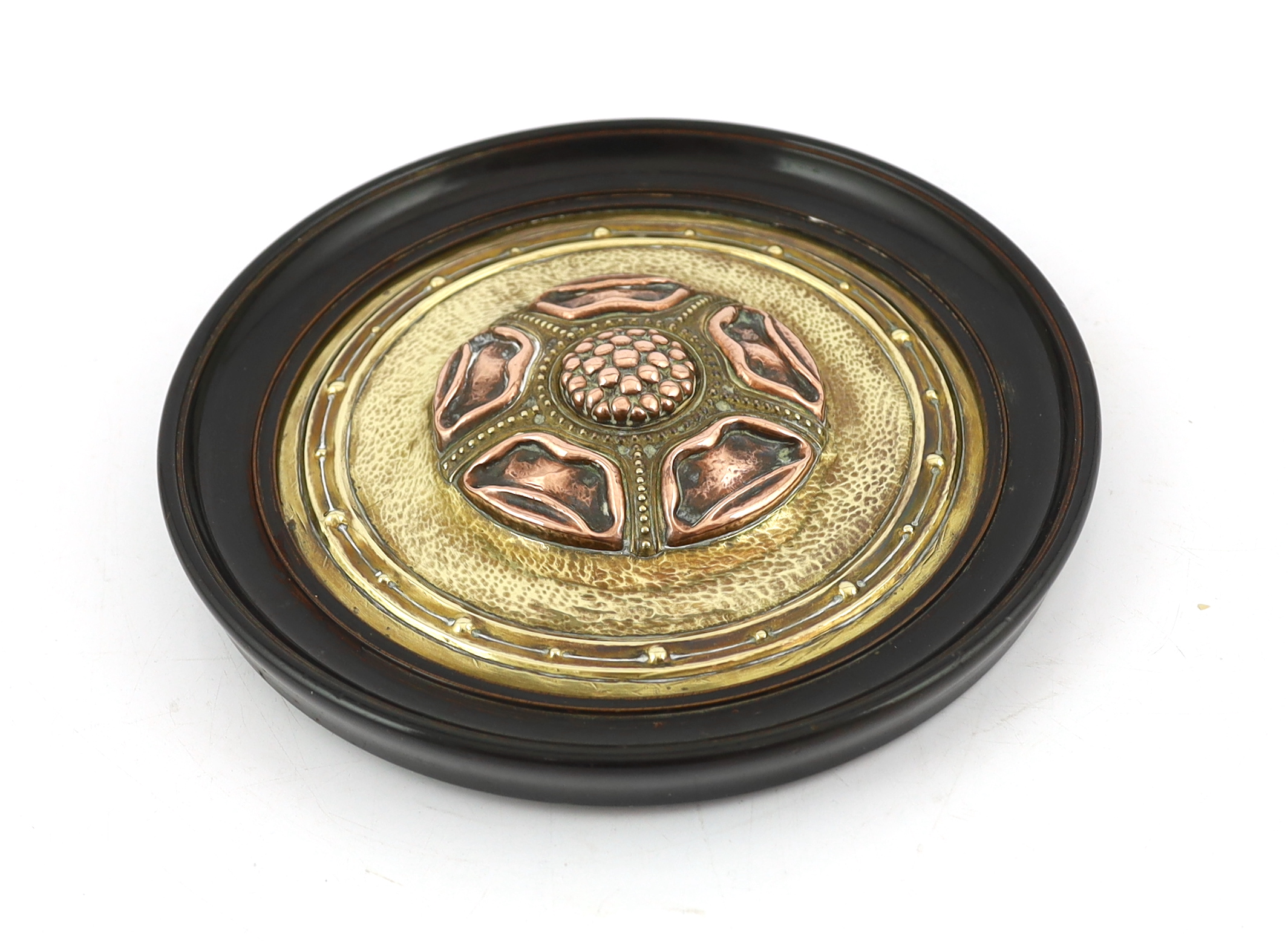An Arts and Crafts brass and copper roundel, in the manner of Archibald Knox, monogrammed CA, ebony framed, overall 27cm